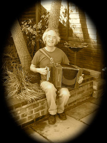 Photo of Tony sitting on small brick wall looking at camera and holding an accordion