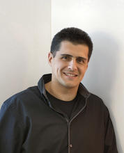 Photo of Gerardo in front of white walls, wearing dark jacket