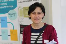 Photo of Orsola in front of maths poster, wearing red cardigan and black and white striped top