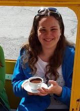 Woman in blue jacket, white top sitting on bench and holding cup and saucer 